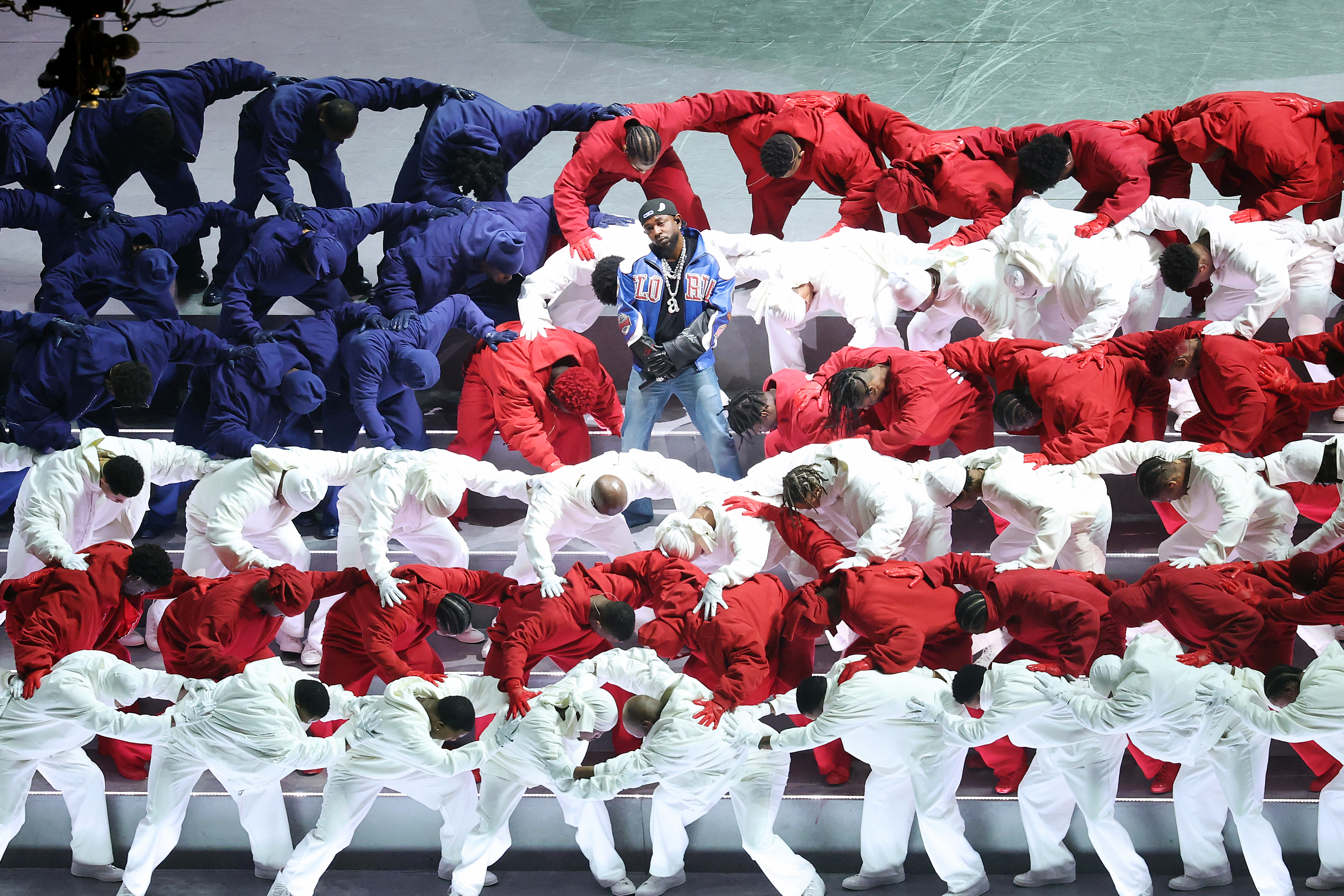 Kendrick Lamar stands among dancers in red, white, and blue outfits, forming a pattern on stage.