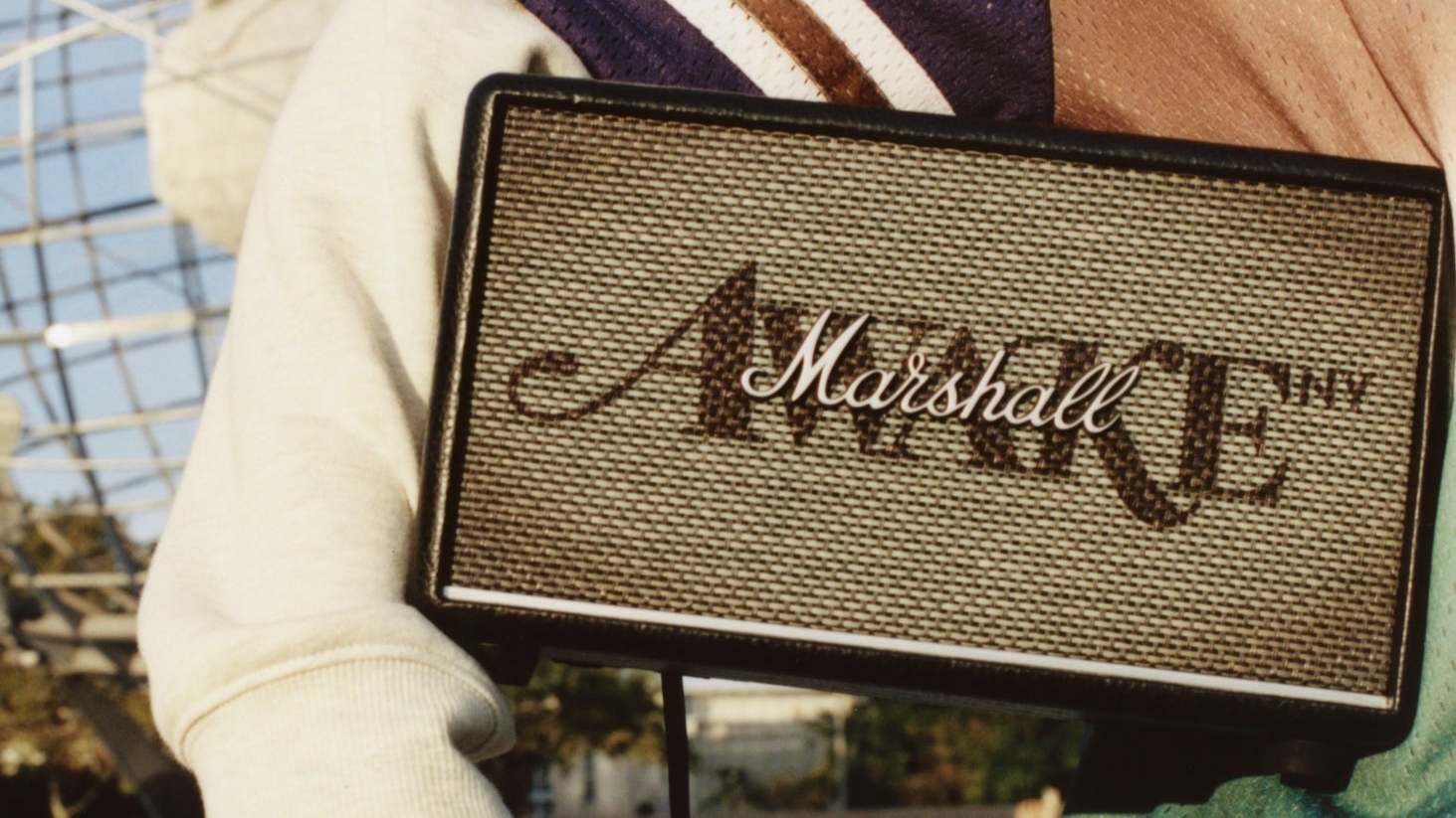A person holding a Marshall speaker with "AWAKE NY" written on it. The background shows part of a large metal structure.