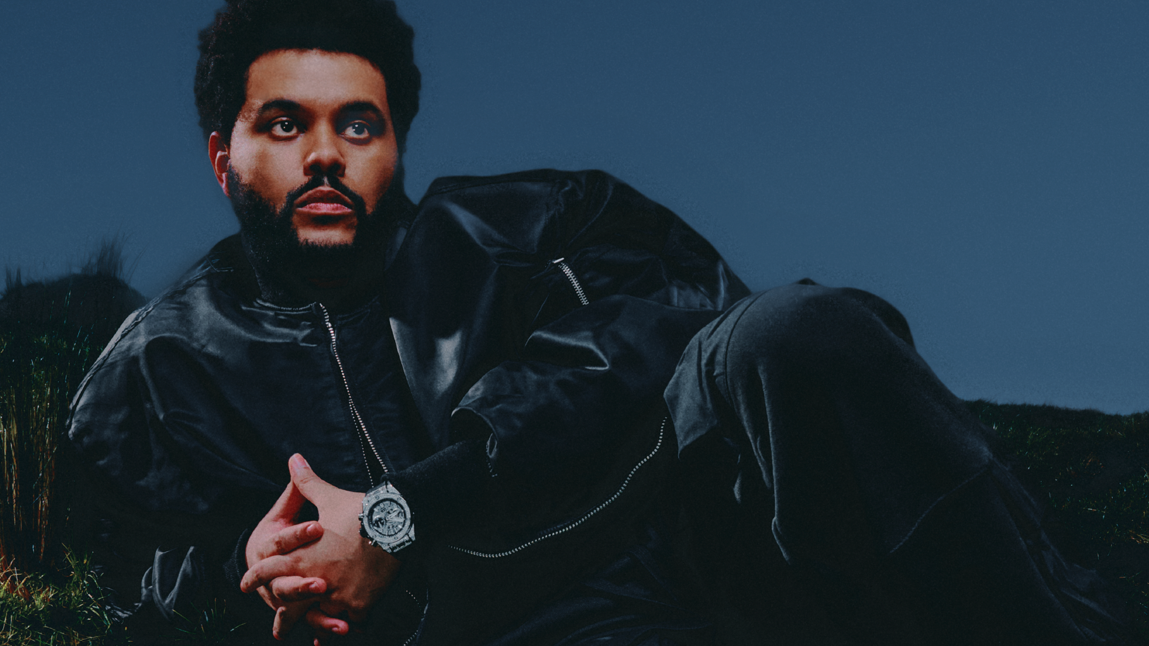 The Weeknd on the cover of Complex magazine, February 2025, wearing a black outfit and sitting on grass.