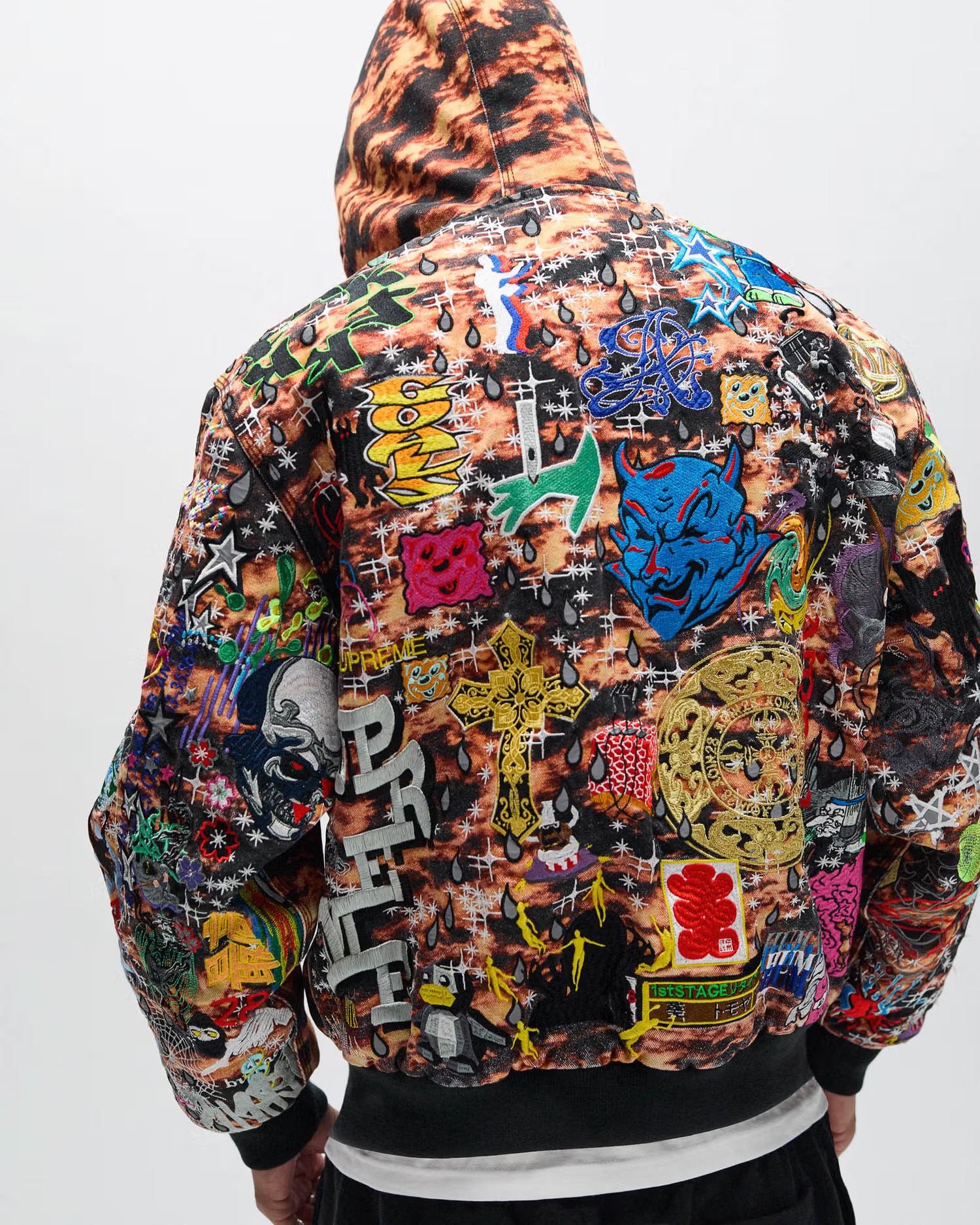 A person wearing a colorful, heavily patterned jacket with various graphic designs and symbols, viewed from the back.